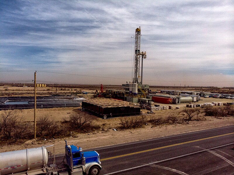 A Semi Truck Hauling Frack Water Drives Past A Drilling Rig Site That Works To Pull Crude Oil And Gas Out Of The Ground To Be Refined