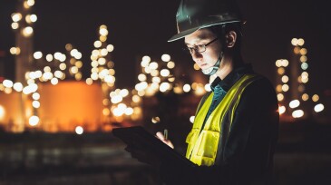 Asian man engineer using digital tablet working late night shift at petroleum oil refinery in industrial estate. Chemical engineering, fuel and power generation, petrochemical factory industry concept