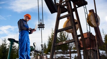 Oil engineer with a laptop standing next to an oil rig making notes in his computer