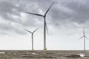 Wind turbines in an offshore wind park during a storm with big waves hitting the shore.