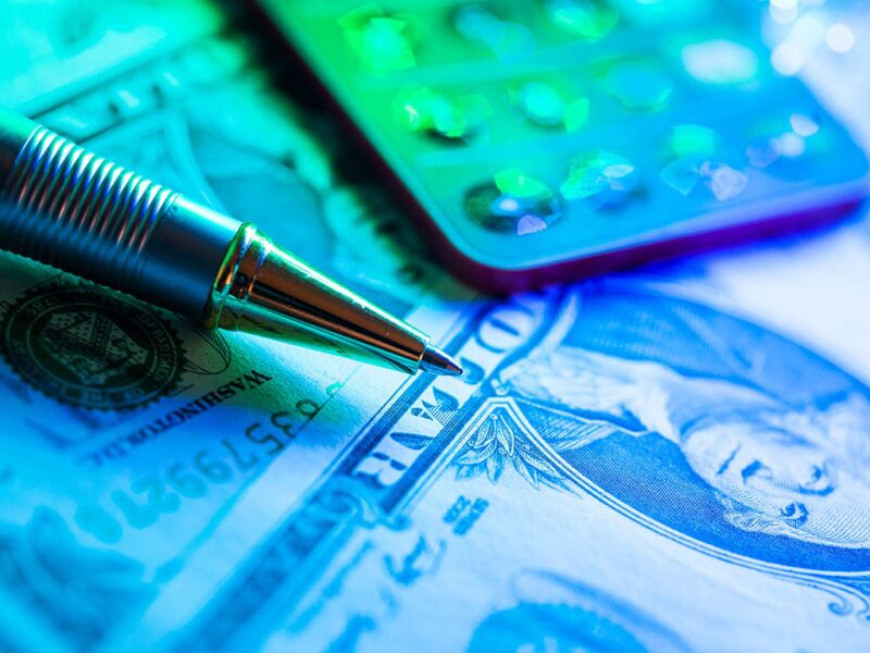 Colored image of a calculator, pen, and dollar