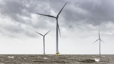 Wind turbines in an offshore wind park during a storm with big waves hitting the shore.