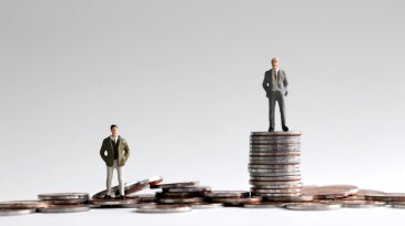 Miniature people standing on a pile of coins.
