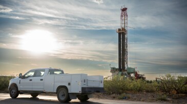Truck passes by an oil drilling platform with a fracking rig in operation, extracting fuel to meet the world's demands