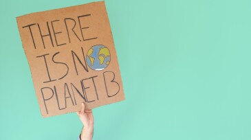 Stop climate change concept. Hand with denim jacket holding a there is no planet b cardboard sign over turquoise background with copy space