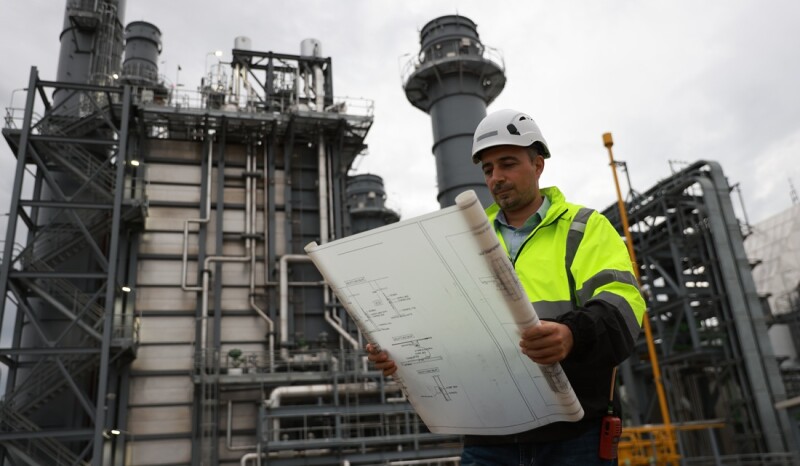 System  engineer with glow green safety jacket holds blueprint drawing at Thermal  Power plant power manufacturing site
