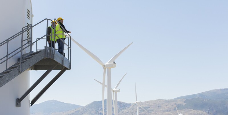 Workers standing on wind turbine in rural landscape