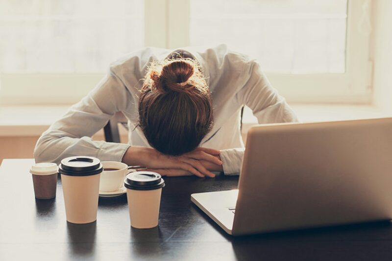 Woman with head on her desk  with computer and cups of coffee nearby