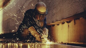 Male worker metal cutting spark on tank bottom steel plate with flash of cutting light close up wear protective gloves and mask