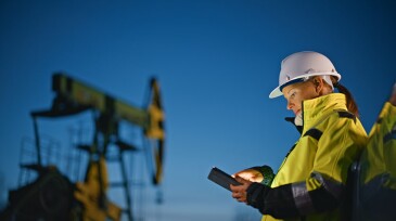 Female worker in protective workwear using tablet PC while standing by car at oil industry against sky