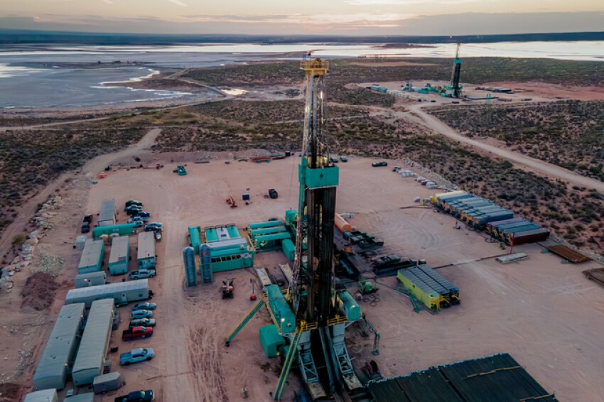 Drone captures a breathtaking sunset over the Permian Basin, showcasing an oil rig drilling and fracking for oil, amidst the vastness of the landscape