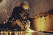 Male worker metal cutting spark on tank bottom steel plate with flash of cutting light close up wear protective gloves and mask