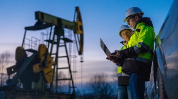 Partners planning over laptop while standing against equipment by car at field