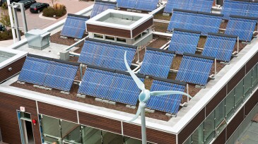 An array of solar panels on the roof of a small building in Halifax, Nova Scotia with a small wind turbine situated nearby.