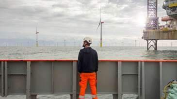 Technician standing on transfer vessel deck in the morning and looking on offshore wind farm and offshore platform around