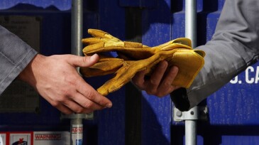 Two men passing gloves beside cargo container, mid section