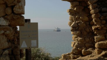 View through the remains of ancient wall, sea tanker at parking