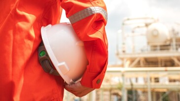 Engineer holding safety helmet with refinery plant.