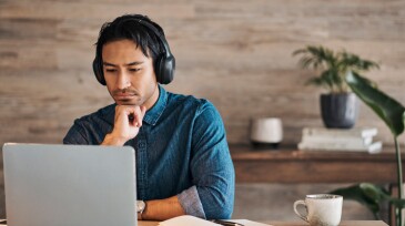 Businessman, headphones and laptop webinar in office with coffee on table, video call or watching video. Zoom call, video conference and male from Canada in online meeting with book and pen on desk.