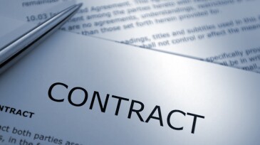 A macro close up blue toned image of a ballpoint pen resting on sheets of legal contract paperwork documents.