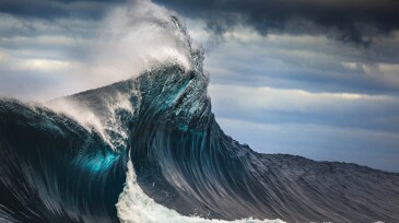 Tall powerful cross ocean wave breaking during a dark, stormy evening.