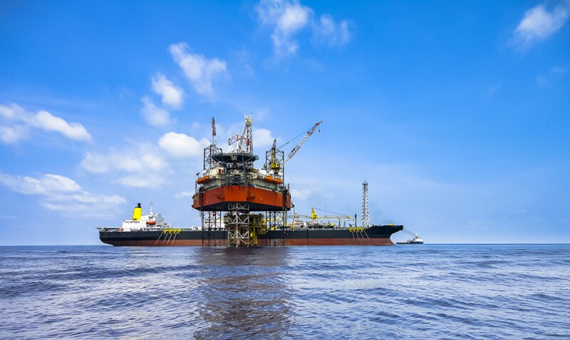 Jack up drilling rig on oil well platform with FPSO ship on site with beautiful cloudy blue sky in offshore oil field