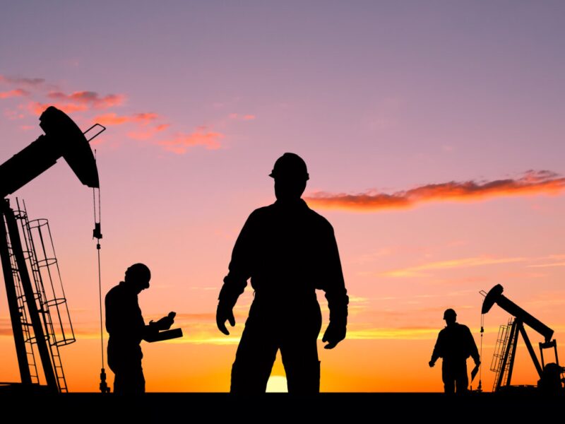 Workers and pumpjacks in silhouette against a sunset sky