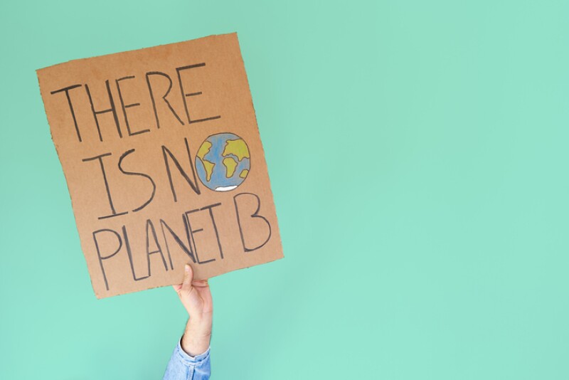 Stop climate change concept. Hand with denim jacket holding a there is no planet b cardboard sign over turquoise background with copy space