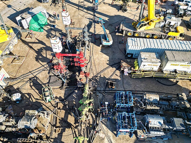 A fracturing site where two large white units from Downing house an automated system that controls the flow of slurry from the pumps into a well during fracturing.