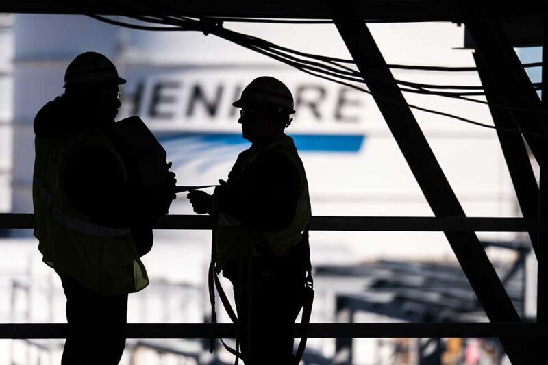 Workers silhouetted against a storage tank with the Cheniere logo