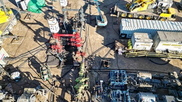 A fracturing site where two large white units from Downing house an automated system that controls the flow of slurry from the pumps into a well during fracturing.