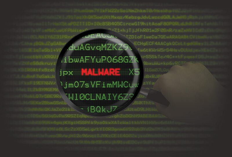 Word "Malware" embedded in computer code viewed through magnifying glass