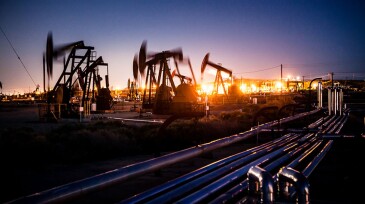 Oil pumpjacks pumping with long exposure motion blur at night as lights glow across the maze of above ground pipelines, Midway-Sunset Oil Field, Kern County, California.