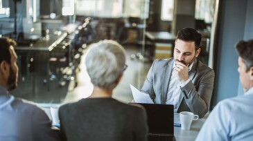 Thoughtful male candidate reading his resume on a job interview in the office.