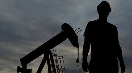 An Oil Industry worker stands in front of a pumpjack.