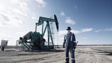 Pumpack,Canada,A man in overalls and a hard hat with a large wrench working at an oil extraction site.