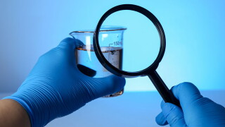 Scientist with magnifying glass and sample of water on light blue background, closeup