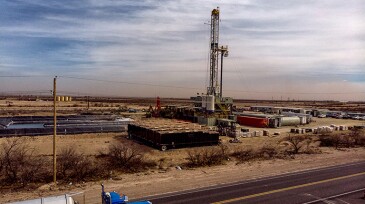 A Semi Truck Hauling Frack Water Drives Past A Drilling Rig Site That Works To Pull Crude Oil And Gas Out Of The Ground To Be Refined