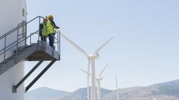 Workers standing on wind turbine in rural landscape
