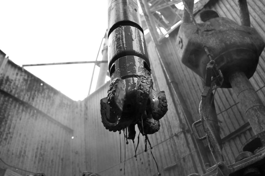 Drilling bit and positive displacement motor in front of drilling rig in black & white